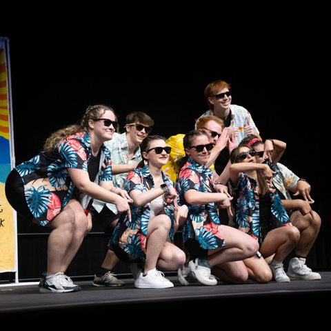 A group of students dressed in matching Hawaiian shirts and sunglasses perform a choreographed dance on stage during the Sycamore Sync Sessions event at Indiana State University.